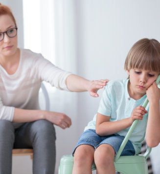 A woman assists a child in sitting on a stool