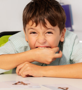 A young boy sits at a table, resting his hands on his mouth