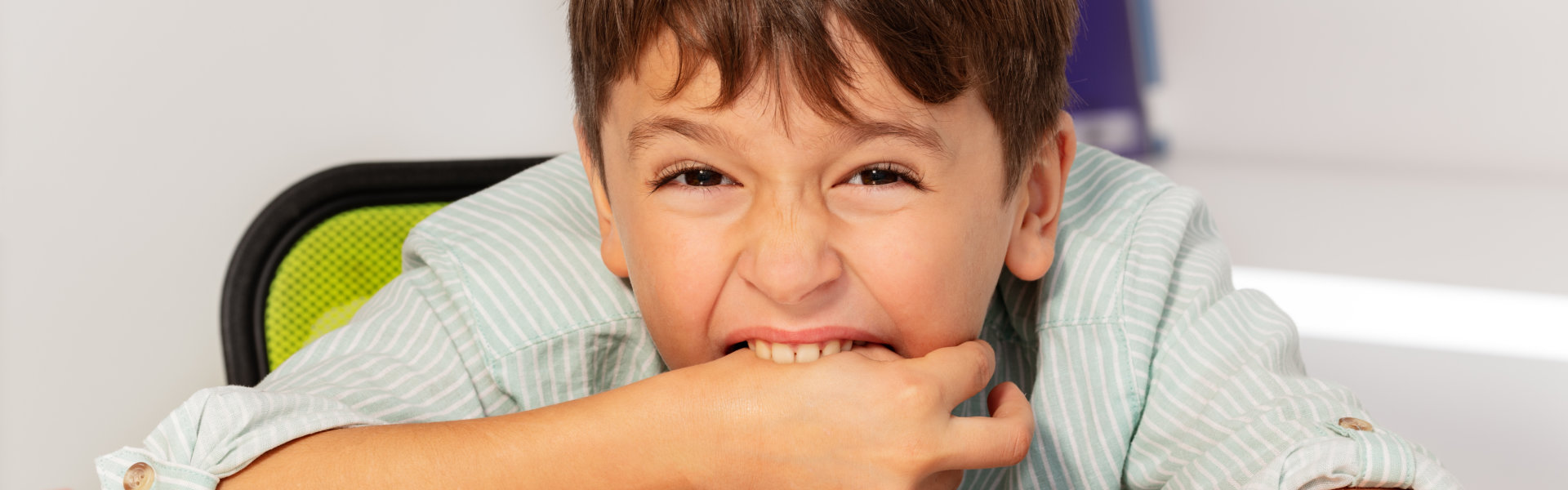 A young boy sits at a table, resting his hands on his mouth